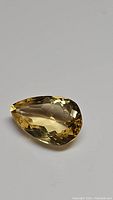 Natural pear cut golden citrine gemstone viewed from top angle on a plain background, showing faceting and clarity.