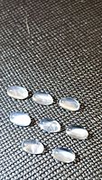 Eight oval cabochon moonstones on textured black surface, showing catseye flash.