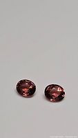 Pair of deep pink oval cut gemstones placed side by side on a plain background.