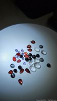 All gemstones arranged under bright light showing variety and color, including red garnets, purple iolites, clear quartz, black onyx, and snowflake obsidian.
