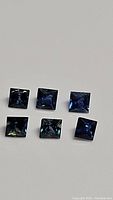 Clear photos of six blue sapphires in princess cut, showing facets and color variations.