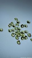 Scattered small apple green round faceted peridot gemstones displaying clarity and color under lighting.