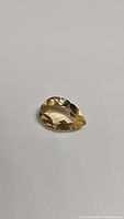 Pear shaped golden citrine gemstone on neutral background showing faceted cut and clarity.