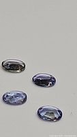 Four natural oval cut tanzanite gemstones showing front side with color and clarity visible on neutral background