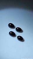 Four oval polished jet black onyx cabochon gemstones on a plain background.