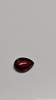 Close-up front angle of deep red pear-shaped garnet gemstone showing its clarity and shape.
