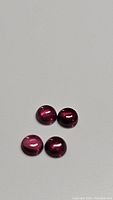 Four round cabochon rhodolite garnet gemstones arranged on a grey surface showing deep pink to purple color and smooth polished domed surfaces.