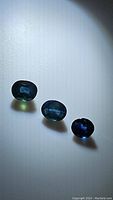 Three oval-shaped natural blue sapphires arranged in a row showing color and size differences under direct light, highlighting their color and clarity.