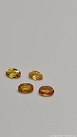 Four natural oval cut Ceylon sapphires showing varying shades of yellow to orange color on neutral background.