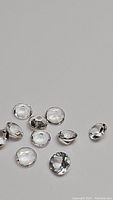 Multiple round cut clear natural crystal quartz stones laid out on a grey surface showing facets and transparency.