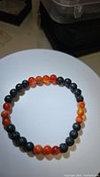 Top-down image of a stretchy gemstone bracelet featuring black lavastone and red agate beads arranged alternately on an elastic band.
