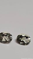 Pair of natural green amethyst (prasiolite) gemstones, oval cut, lying side by side on plain surface showing facets and clarity.