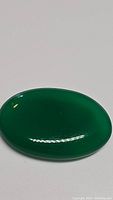 Close-up photo of the oval cabochon green onyx gemstone showing its vivid green color and polished surface.