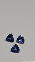 Three natural tanzanite gemstones in trillion cut set against a white background showing their blue to purple hues and facets.