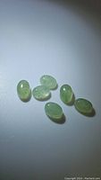 Six oval cabochon mint green kyanite gemstones arranged on white surface under light to show translucency and color.