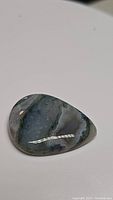 Photo of polished pear-shaped moss agate cabochon gemstone with visible moss-like dendritic patterns inside the stone