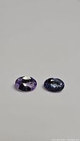 Two oval cut tanzanite gemstones, purple and blue colors, shown side by side on neutral background.