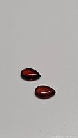 Two pear-shaped cherry red garnet cabochon gemstones displayed on a plain surface showing their smooth polished finish and deep red hue.