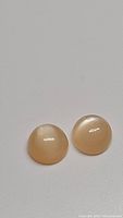 Two round peach moonstone cabochons side by side on grey background, showing glossy smooth surfaces and soft peach color.