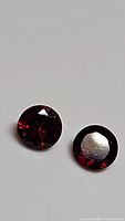 Pair of round faceted deep red pyrope garnet gemstones showing front and back with reflective diamond cut facets.