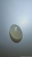 Close-up photo of natural pearl white moonstone oval cabochon gemstone on a plain background, showcasing its translucent white color and smooth polished surface.