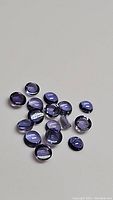 Multiple natural purple iolite cabochon gemstones on a neutral background, close-up showing color and cut.