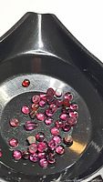 Photo showing multiple small round rhodolite garnet cabochon gemstones in pink-purple hues with calibrated sizes on a black tray.