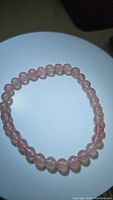 Strawberry quartz bead bracelet laid out flat on a white round surface, showing polished translucent pinkish beads strung together.