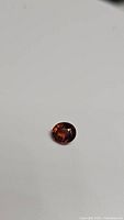 Oval cut tourmaline gemstone with a deep orange color displayed on a white background.