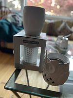 Three Yankee Candle warmers including a boxed textured white ceramic warmer, clear glass warmer with chevron pattern, and white ceramic owl-shaped warmer.