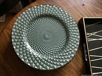 Set of 8 clear textured glass plate chargers with overlapping teardrop pattern, laid out on wooden table, showing design details