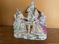 Front view of the porcelain sculpture showing two seated women and a standing man playing chess.
