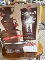 Front of box showing Wilton Chocolate Pro Chocolate Fountain with product image, strawberry and chocolate flow, indicating 4-pound capacity