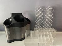 Photo showing a black plastic and silver mesh metal hair dryer holder, two clear acrylic lipstick holders with grid compartments, and a clear clear acrylic organizer for brushes or lip gloss.