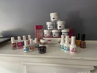 Various dip powder nail products including jars, liquid bottles, polish, brushes and nail tips arranged on a white surface against gray background.
