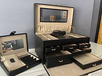Photo shows a black Gunther Mêle jewellery box opened to reveal compartments lined with beige fabric, a large mirror inside the lid, multiple small drawers and pull-out tray drawers with gold-tone handles.