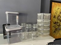 Photo showing various kitchen storage containers including three OXO pop containers in different sizes, six clear glass jars with silver screw lids, and a set of five small plastic containers with snap lids stacked.
