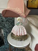 Full view of the vintage lamp with a porcelain lady figurine base and pink fabric shade