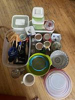 Overview shot showing all kitchen items spread on floor including chip maker, bowls, mugs, utensils, and containers.