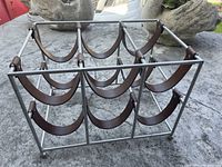 Metal and leather wine rack showing six individual curved leather slings attached to a rectangular grey metal frame, designed to hold wine bottles horizontally.