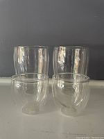 Four clear double-walled glass cups, two larger and two smaller, all in good condition, set against a dark background.