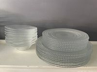 Set of clear glass bowls and plates with hobnail dot relief pattern stacked on a white surface