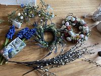 Photo showing artificial spring floral wreaths, Easter-themed wreath, and loose flower and willow stems arranged on wooden surface.