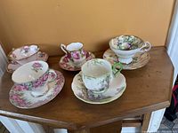 Photo showing five different bone china teacups and saucers with floral patterns arranged on a wooden table.
