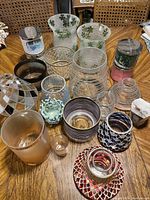 Overview of various glass candle holders arranged on a wooden table, showing different sizes and styles including large clear ribbed holders, frosted, and mosaic holders.