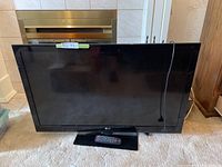 Front view of the LG flat screen TV on black base with universal remote placed on the base.