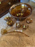 Photo of punch bowl, 7 cups, ladle on carpet with dresser background showing iridescent amber carnival glass and leaf pattern