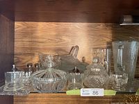 Shelf view of assorted crystal and glass serving pieces including covered dishes, glass bowls, and small serving items.