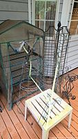 Full view of mini greenhouse with clear plastic cover and metal frame alongside an assortment of metal plant trestles and garden supports on wooden deck.