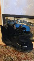 Black cowboy boots, felt cowboy hat, and Pony Express painted mirror arranged on a patterned rug.